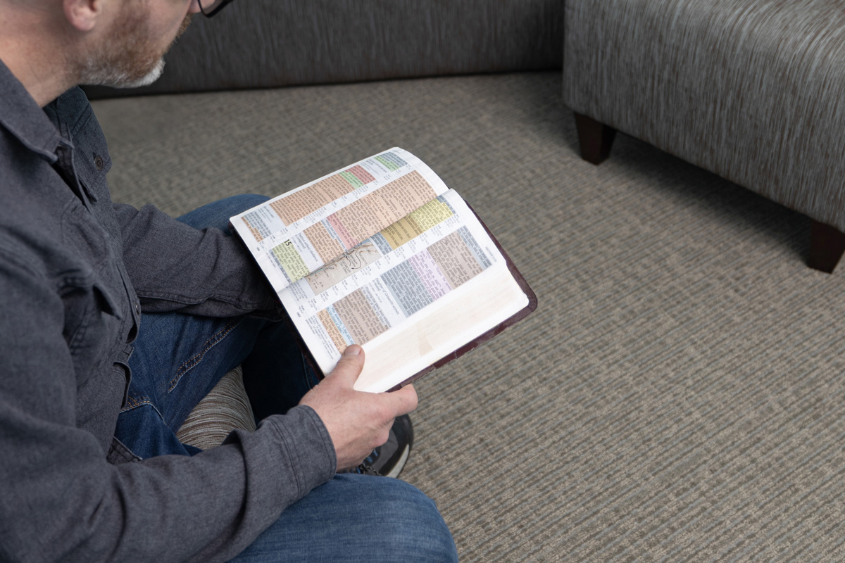 Man sitting on a couch reading a book with highlighted and underlined text.