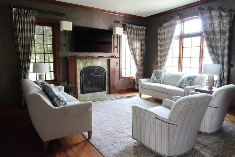 Elegant living room with white sofas, armchairs, a fireplace, large windows, and patterned curtains.